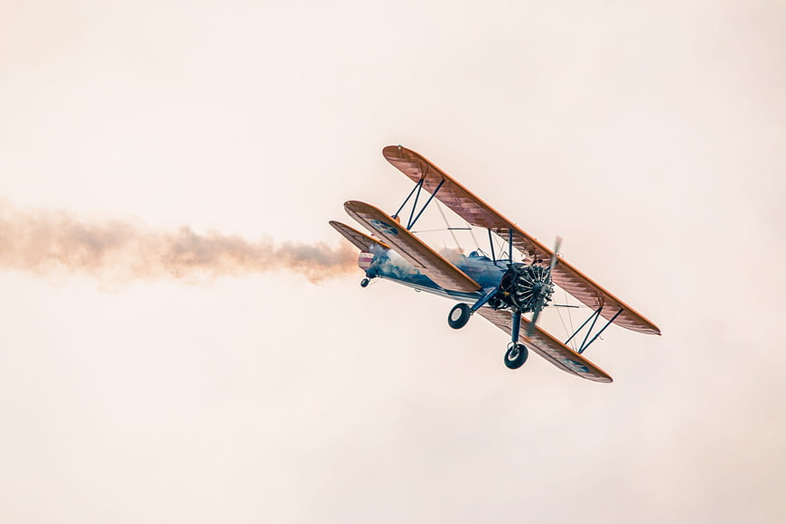 Vintage biplane performing aerial stunt with smoke trail
