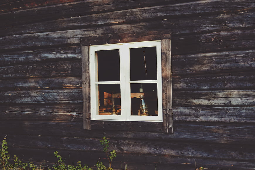 White window on weathered dark wooden log cabin wall