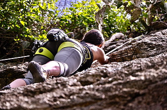 Woman rock climbing on rugged terrain with harness