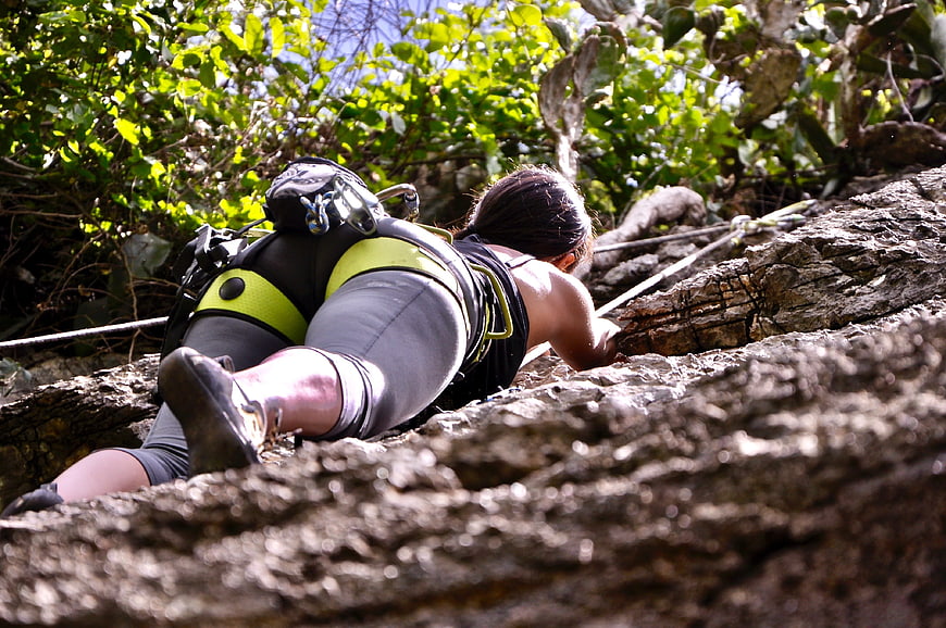 Woman rock climbing on rugged terrain with harness