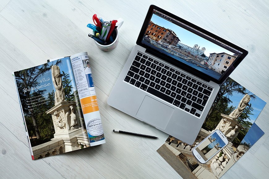 Flat lay of laptop, magazine, and smartphone displaying travel photos