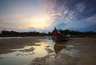 Colorful fishing boat on sandy beach at sunset with reflection