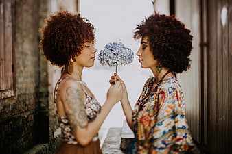 Two women with afro hair holding blue hydrangea flower
