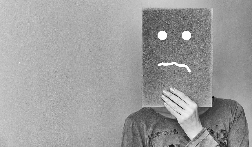 Person holding sad face cardboard mask against gray wall