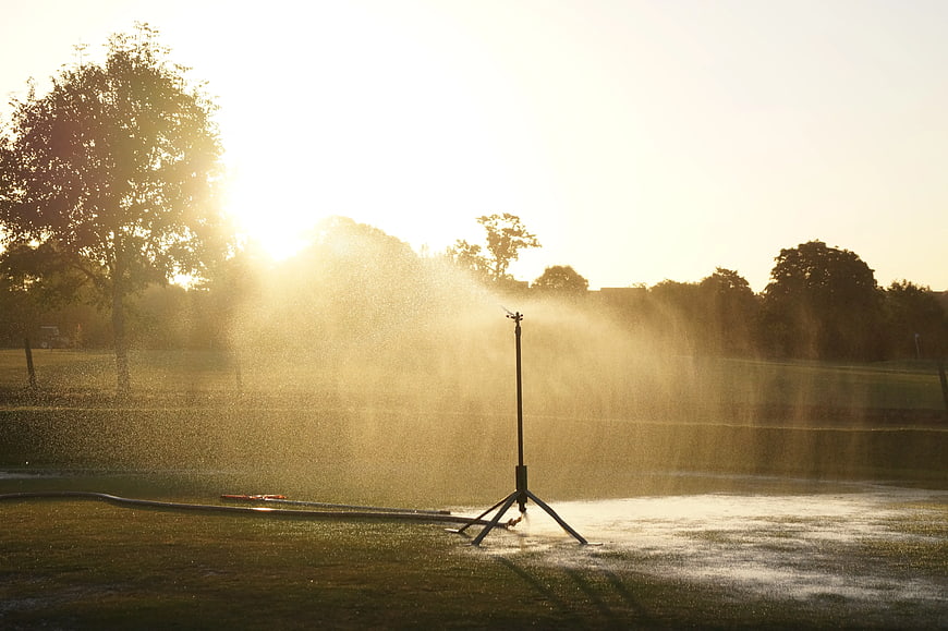 Sprinkler watering grass field at golden hour sunset