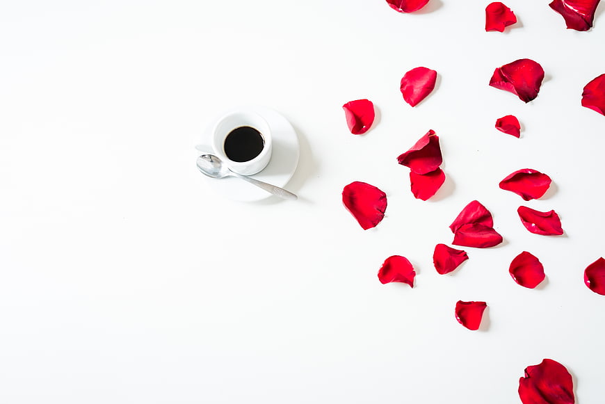 Flat lay of black coffee and red rose petals on white background
