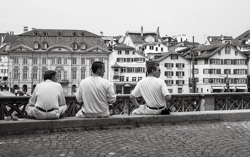 Three Men Sitting on Bridge in Black and White Cityscape