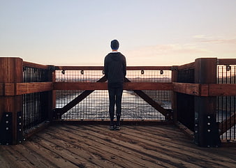 Man Standing on Wooden Deck Overlooking River at Sunset