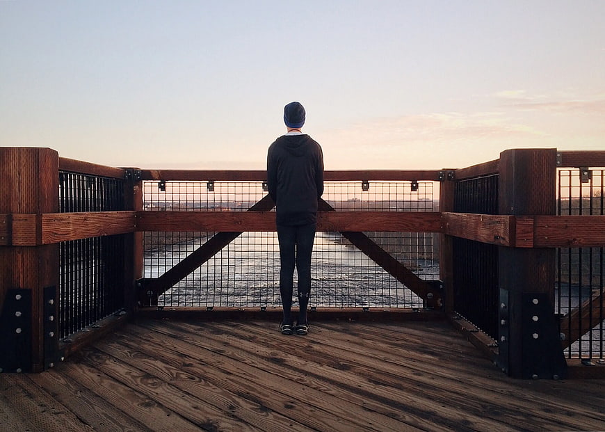 Man Standing on Wooden Deck Overlooking River at Sunset
