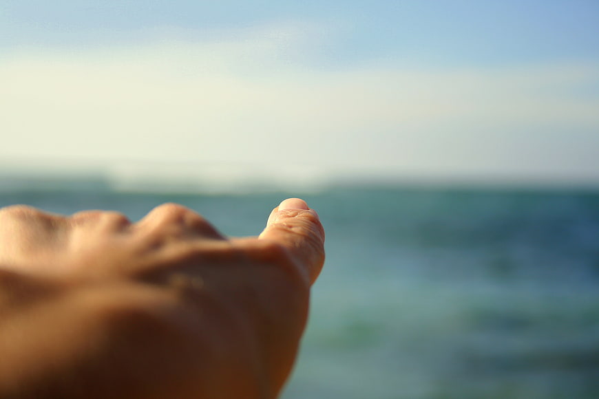 Close-up of hand pointing toward ocean horizon