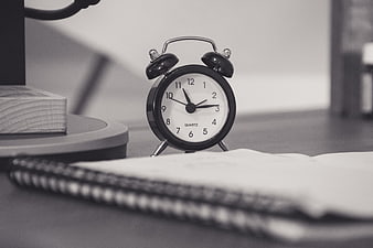 Black and white alarm clock on desk with notebook