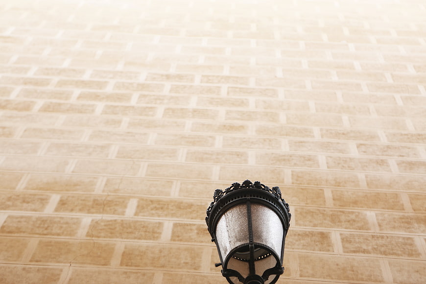 Low angle view of ornate black street lamp against beige brick wall