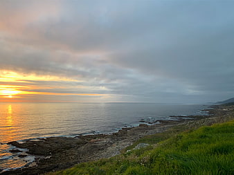 Dramatic Sunset Over Rocky Coastline with Green Grass