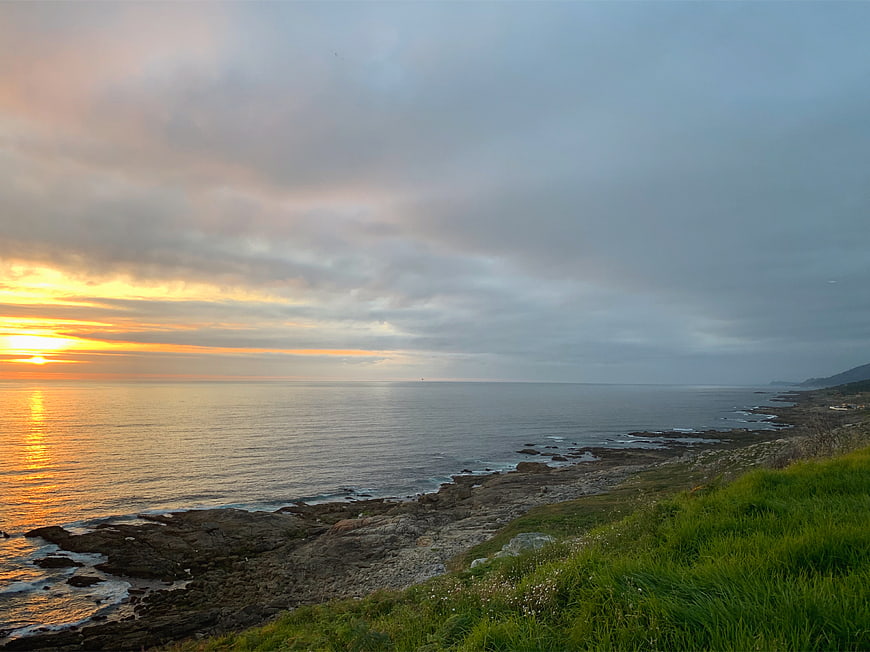 Dramatic Sunset Over Rocky Coastline with Green Grass