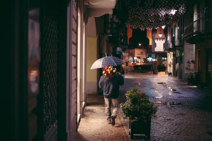 Man Walking with Flowers and Umbrella on Rainy Night Street