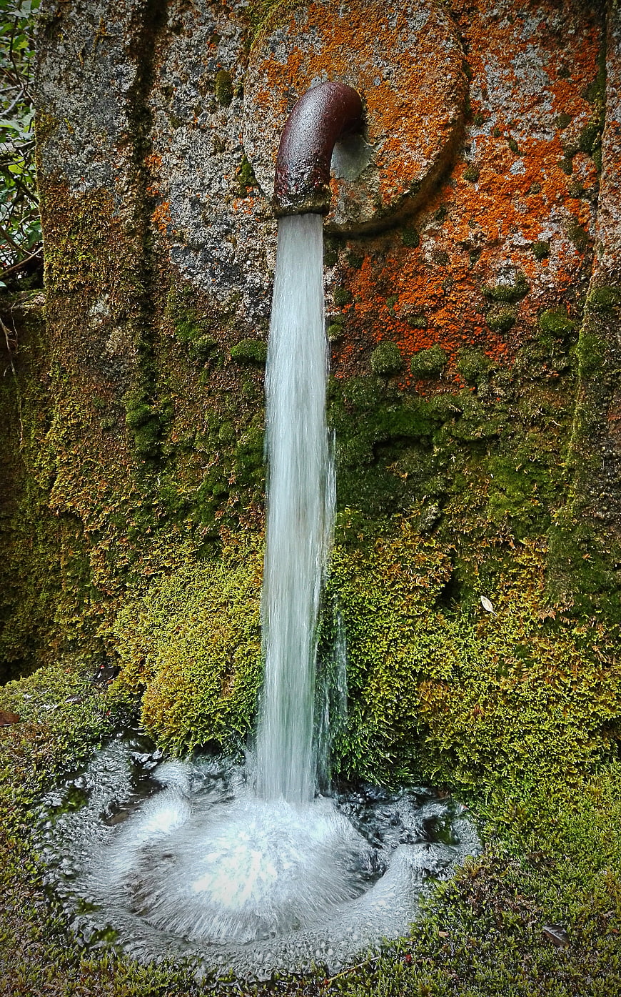 Old Iron Pipe Spouting Water Into Mossy Stone Fountain