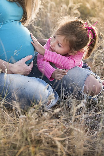 Toddler Girl Listening to Pregnant Mother's Belly in Field