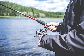 Close-up of hands holding fishing rod by lake