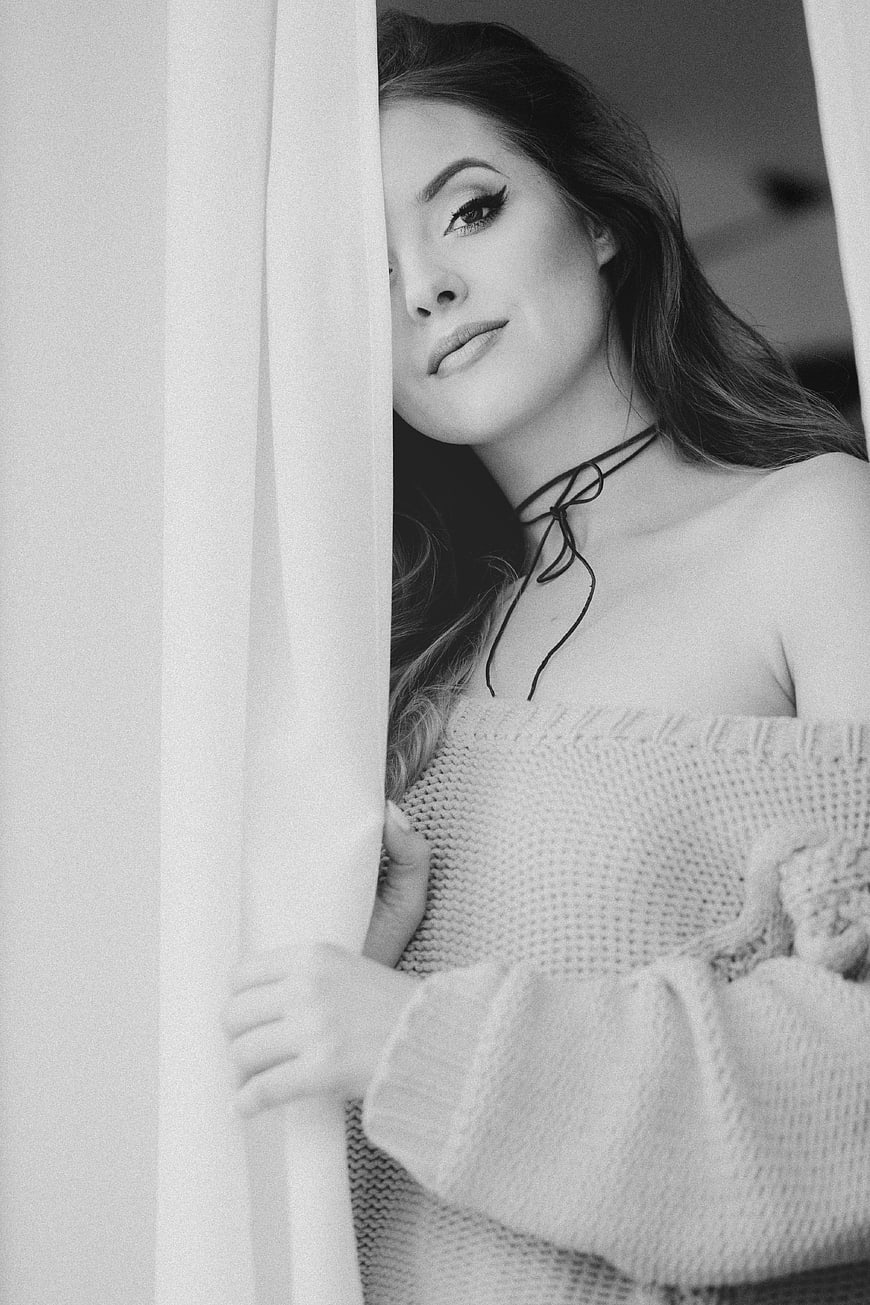 Black and white portrait of woman peeking from behind curtain