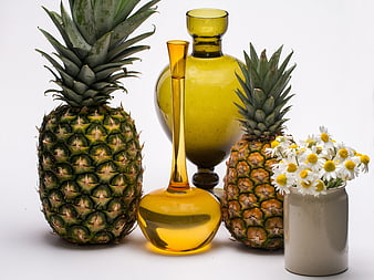 Still life with pineapples, amber glass vases, and daisies on white background