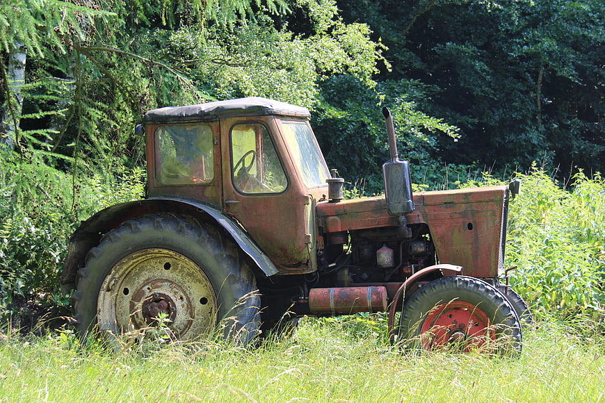 Rusty vintage tractor abandoned in overgrown green field