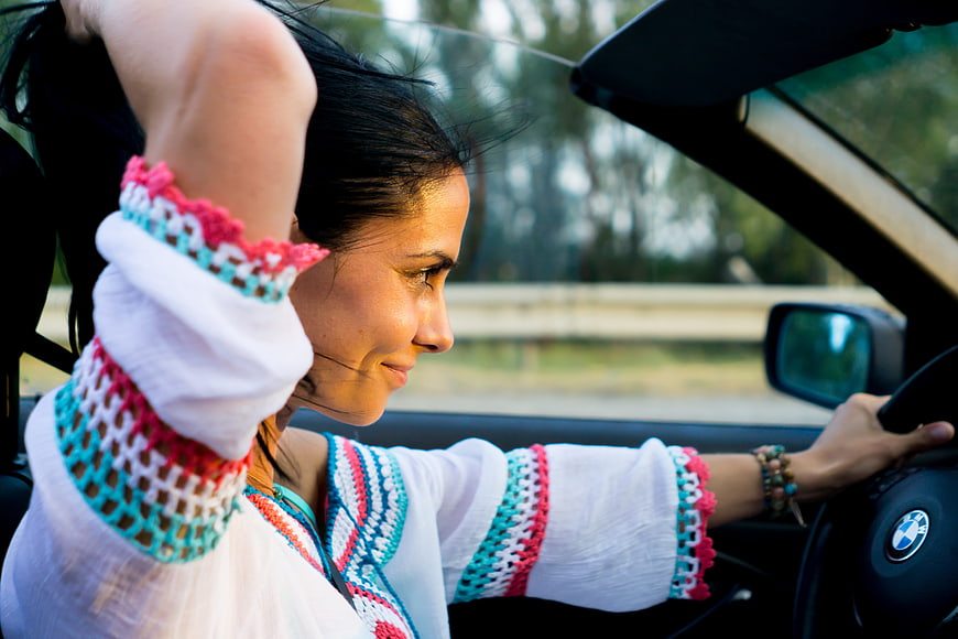 Happy woman driving convertible car with colorful crochet top