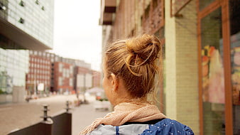 Woman with blonde bun looking at city street
