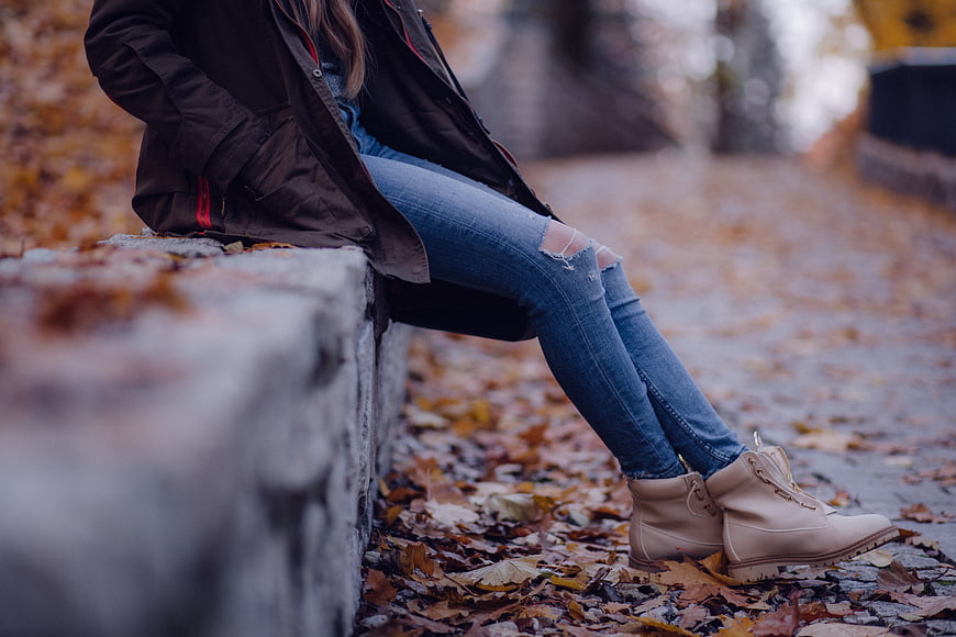 Woman in ripped jeans and boots sitting on autumn leaves