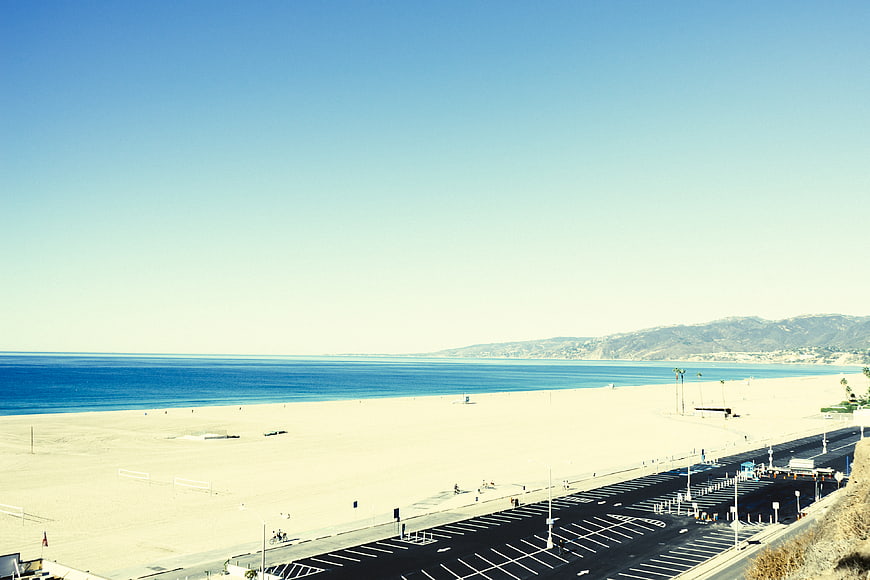 Wide coastal view of sandy beach, blue ocean, and parking lot