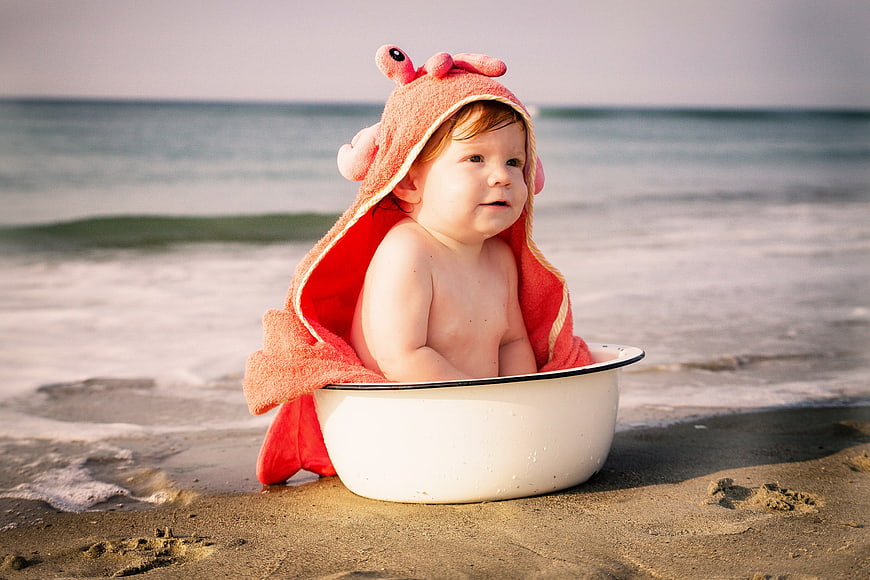Baby in Crab Hoodie Sitting in White Basin on Beach