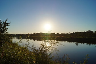 Serene River Landscape with Sun Reflection and Forest Horizon