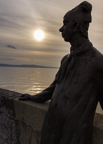 Bronze Statue Silhouette Against Sunset Over Lake