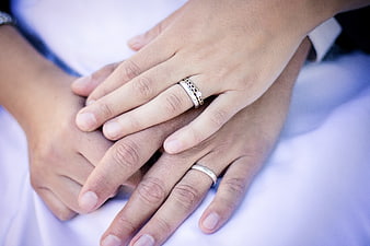 Close-up of interlocked hands wearing wedding rings on white fabric
