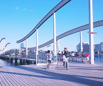 People walking on modern wooden boardwalk bridge in Barcelona
