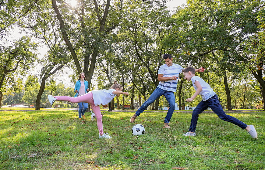 Happy family playing soccer together in a sunny park