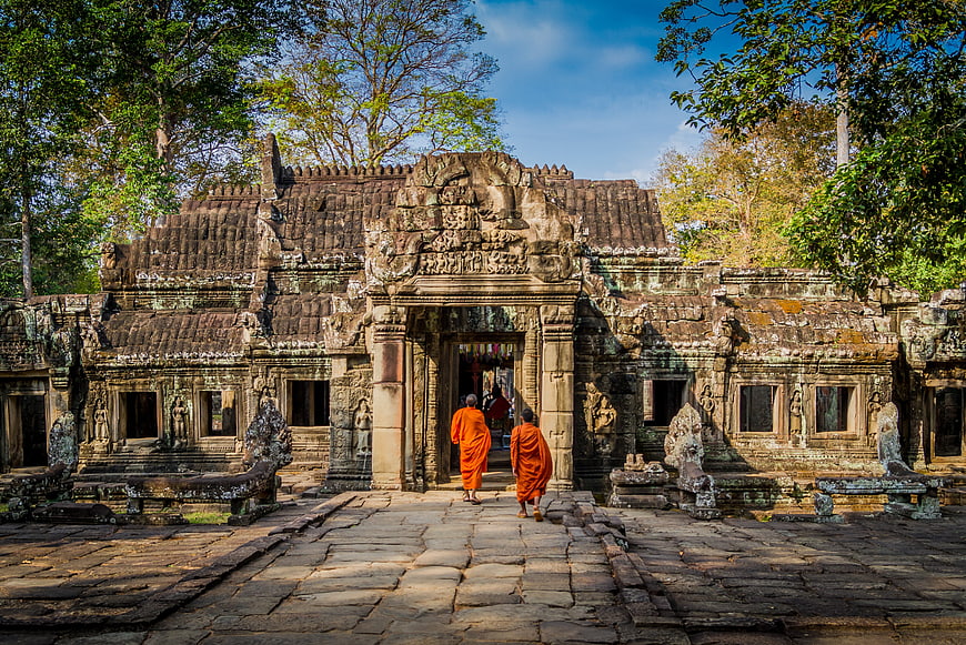 Monks in Orange Robes Walking Through Ancient Khmer Temple Ruins in Cambodia