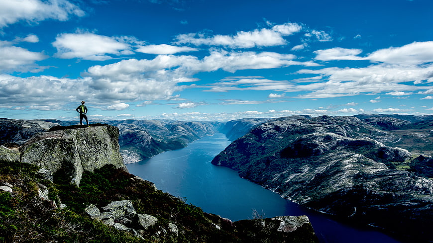 Hiker standing on cliff overlooking fjord landscape