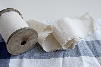Vintage wooden spool with white cotton fabric on blue checkered cloth