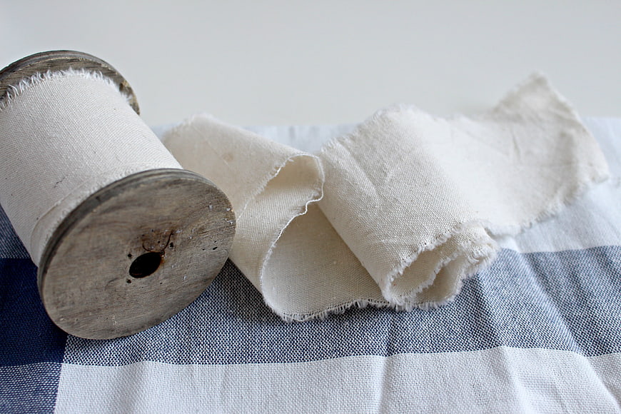Vintage wooden spool with white cotton fabric on blue checkered cloth