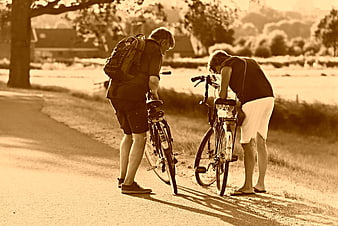 Two cyclists inspecting bicycles on a rural road