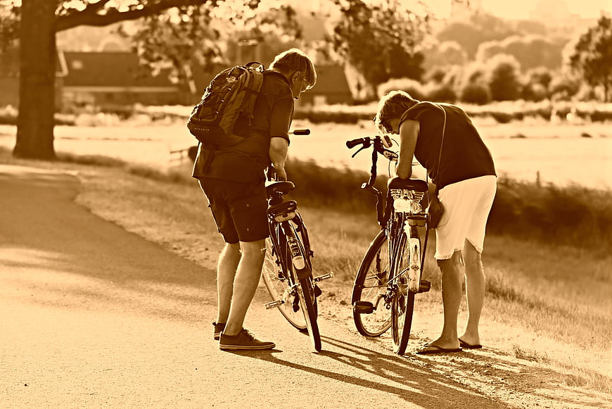 Two cyclists inspecting bicycles on a rural road