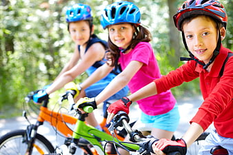 Three happy children cycling together in a park