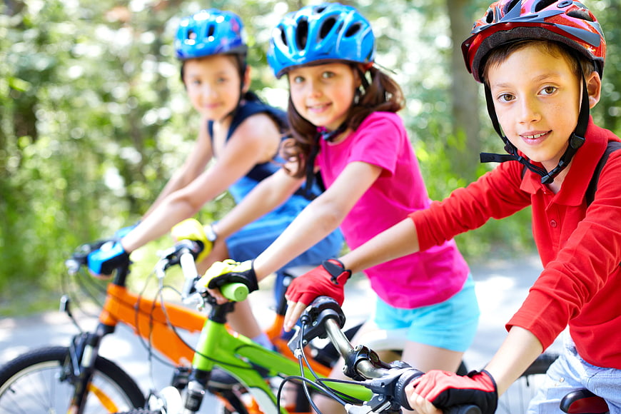 Three happy children cycling together in a park