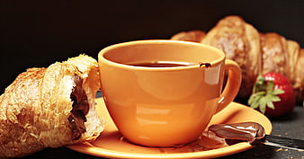 Orange coffee cup with chocolate croissant and strawberries on dark background