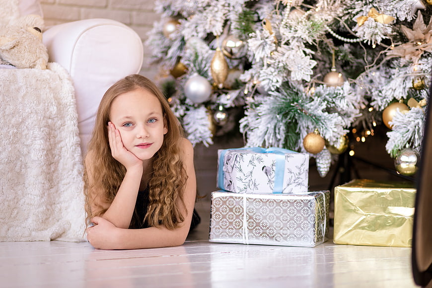 Cute Girl Lying by Christmas Tree with Gifts