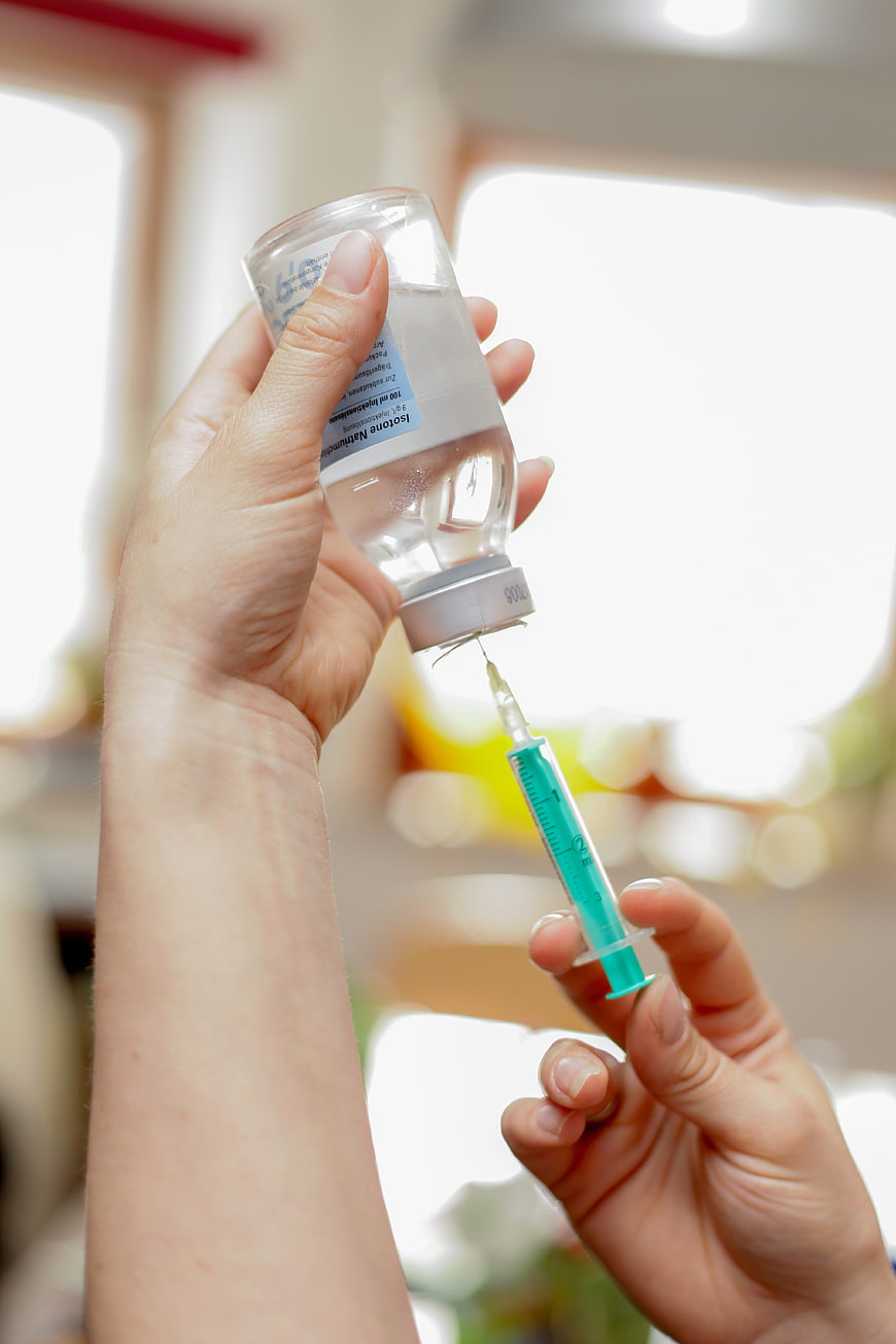Close-up of hands drawing saline solution into a syringe