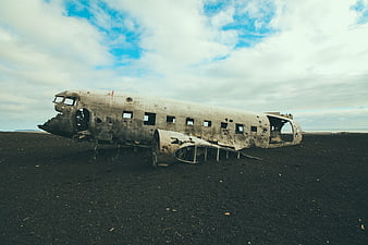 Crashed airplane wreck on black sand beach under cloudy sky