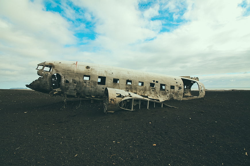 Crashed airplane wreck on black sand beach under cloudy sky