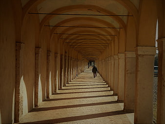 Solitary figure walking through a long arched colonnade