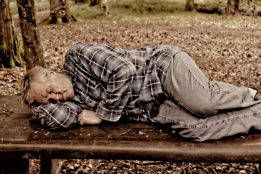 Senior man sleeping on a wooden park bench in a forest
